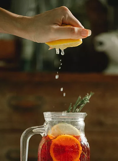 Squeezing a lemon into into a jar containing tea and lemon slices